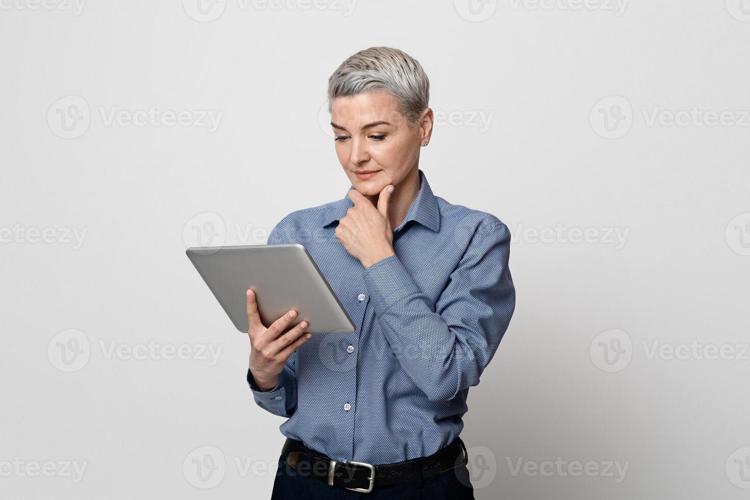Business Applications. Portrait Of Middle Aged Woman Entrepreneur Using Digital Tablet, Standing Over Light Background In Studio, Copy Space photo