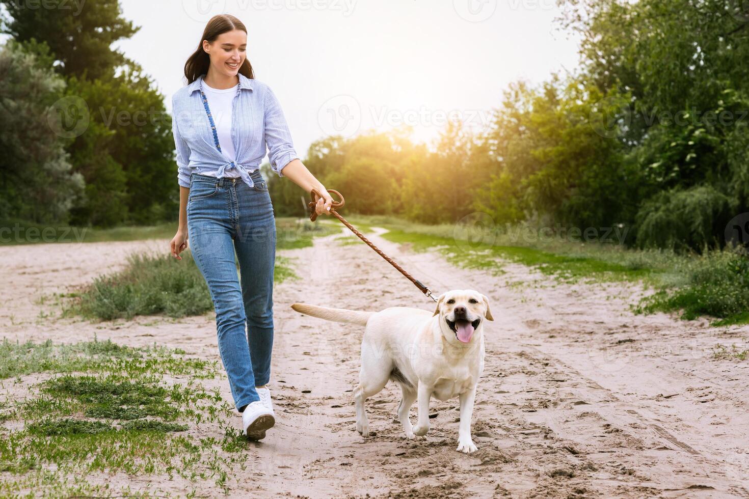 Healthy Lifestyle Concept. Excited girl and her golden retriever walking in countryside, dog is on a leash, free space photo