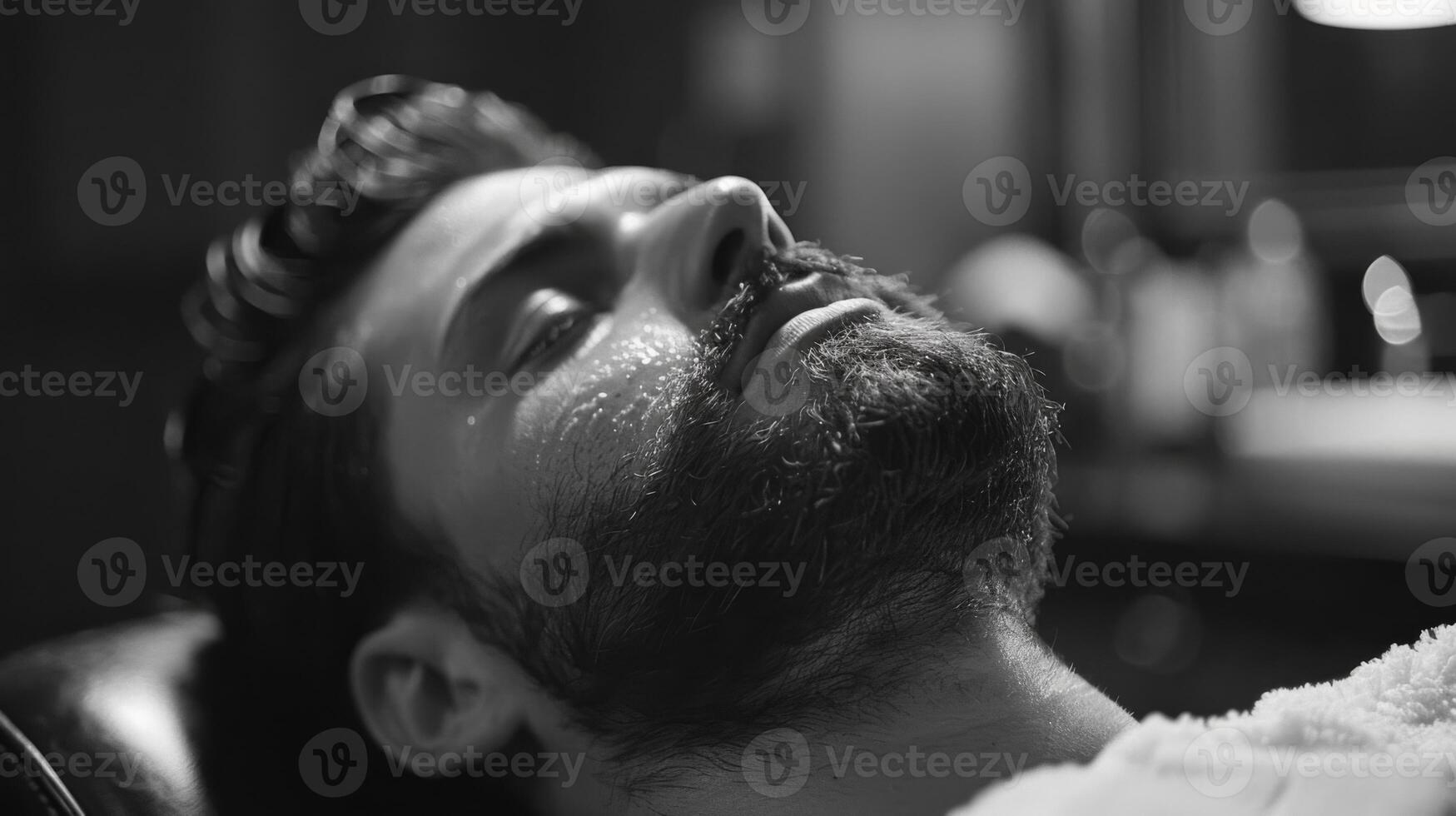 A man with a beard enjoys a grooming session in a barbershop, lying back in a chair while a barber works on his facial hair, creating a calming atmosphere. photo