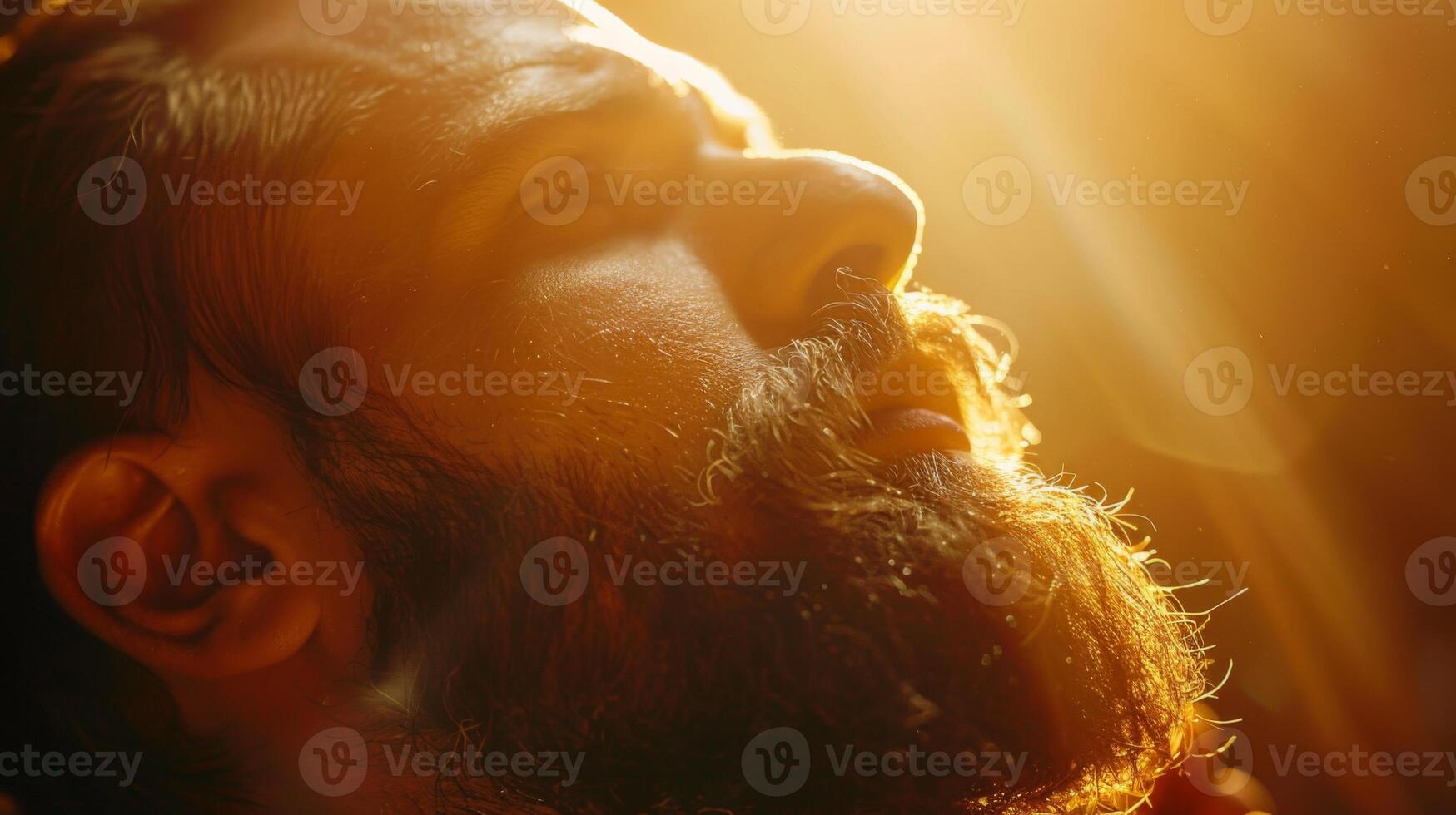 A man is basking in warm sunlight, allowing the golden rays to illuminate his face and beard, conveying a sense of peace and deep thoughtfulness. photo