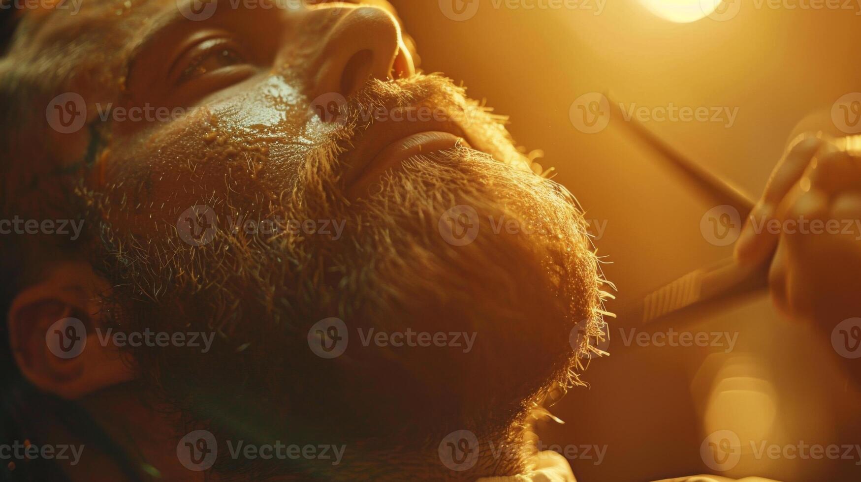 A man relaxes in a barbershop as a barber carefully trims his beard under warm, glowing lights. The setting showcases a calm atmosphere, perfect for grooming. photo