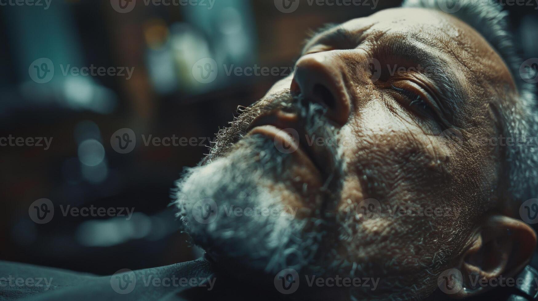 A relaxed mature man lies back in a barbershop chair while receiving a grooming treatment. Subtle reflections of warm lights create an intimate atmosphere. photo