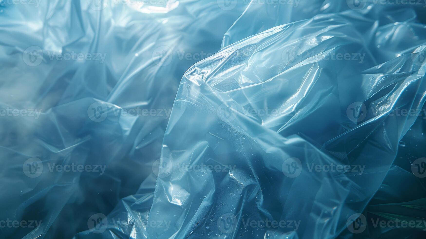 Translucent blue plastic sheets are piled and wrinkled, reflecting sunlight and casting intricate shadows while revealing layers that suggest depth and texture in a natural environment. photo