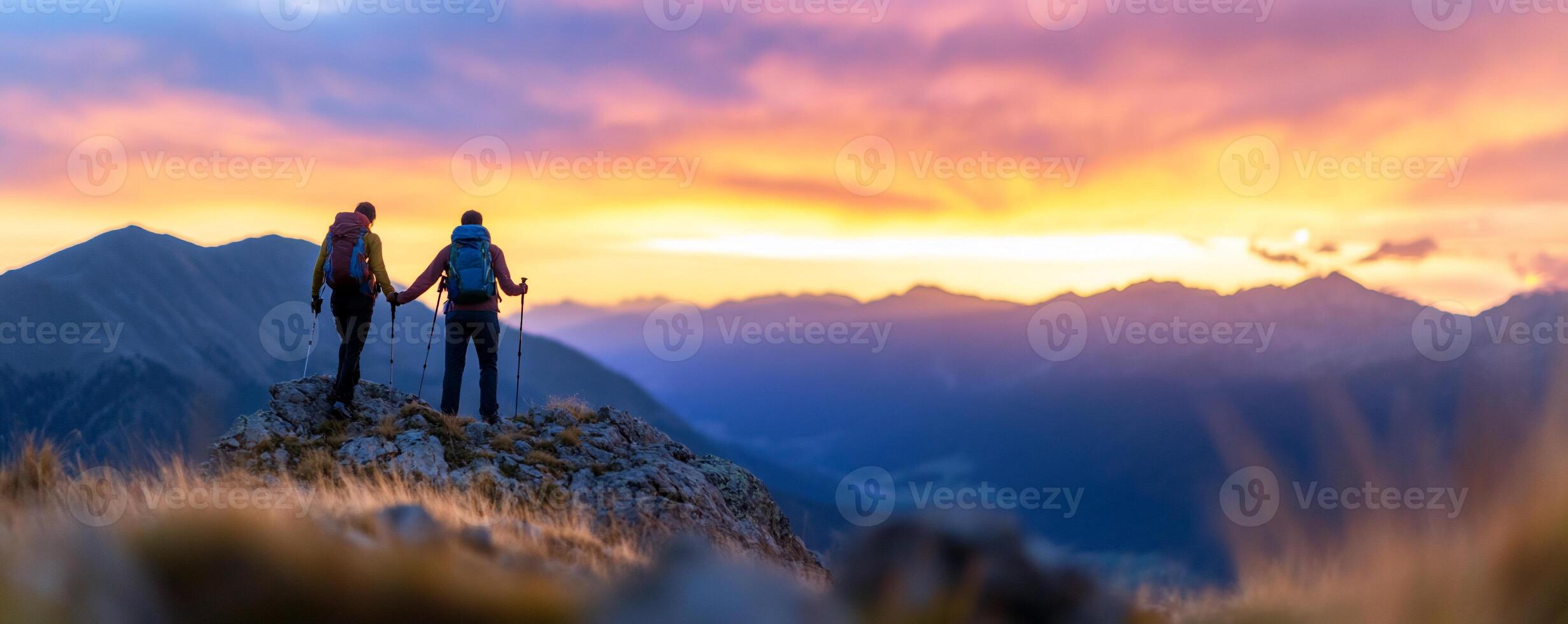 Two hikers holding hands at sunset on a mountain peak. photo