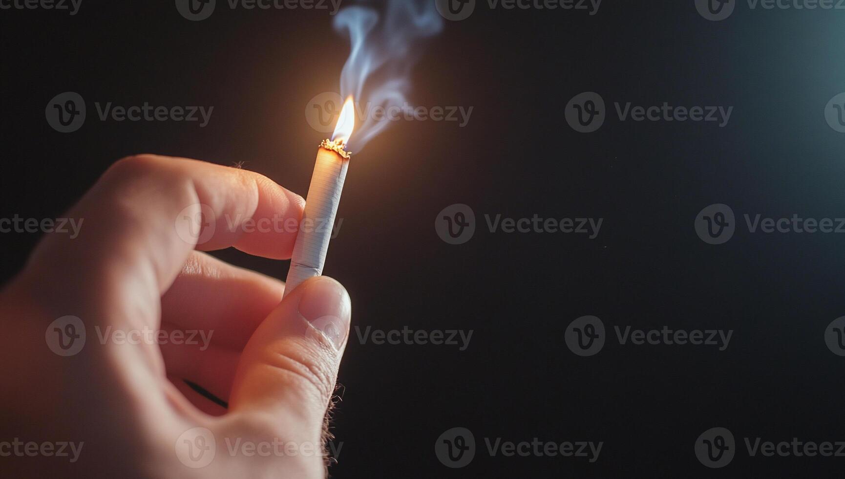 A hand holding a lit cigarette with smoke curling upwards. photo