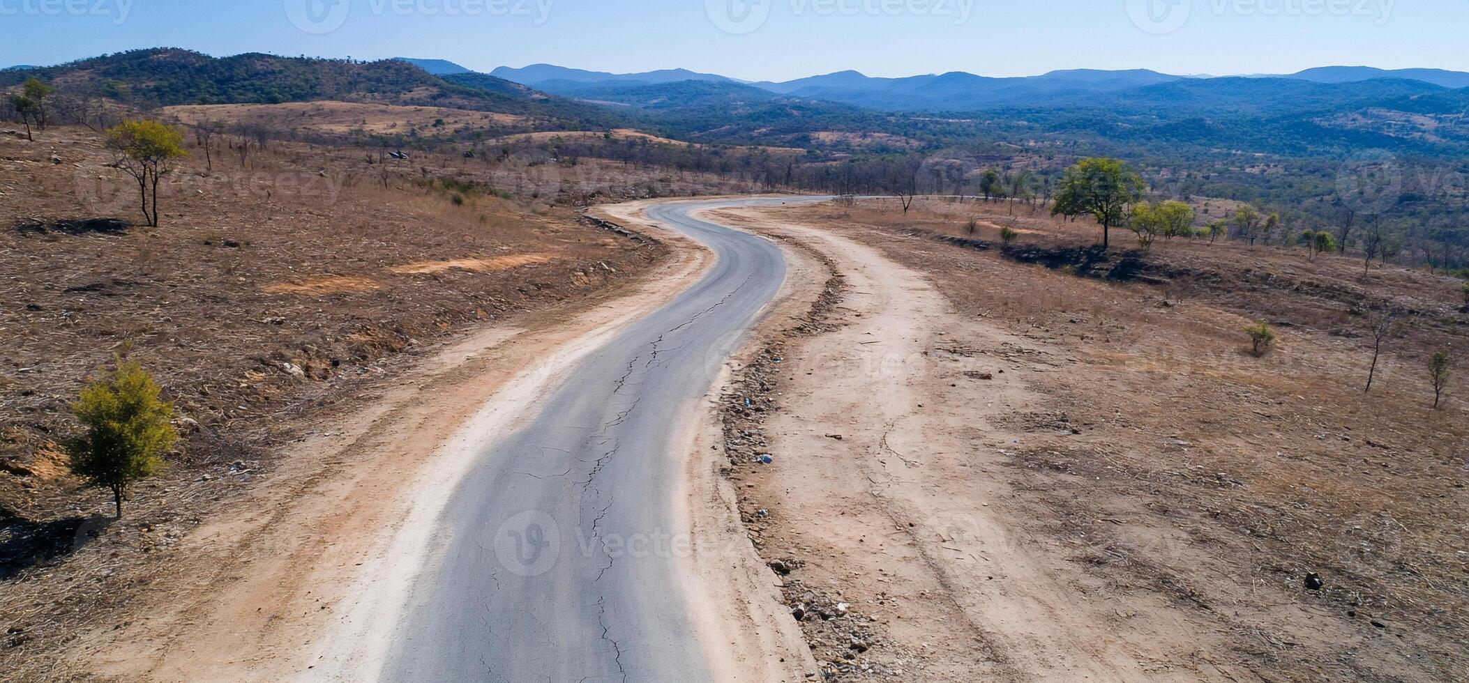 A winding road through a dry, barren landscape under a clear sky. photo