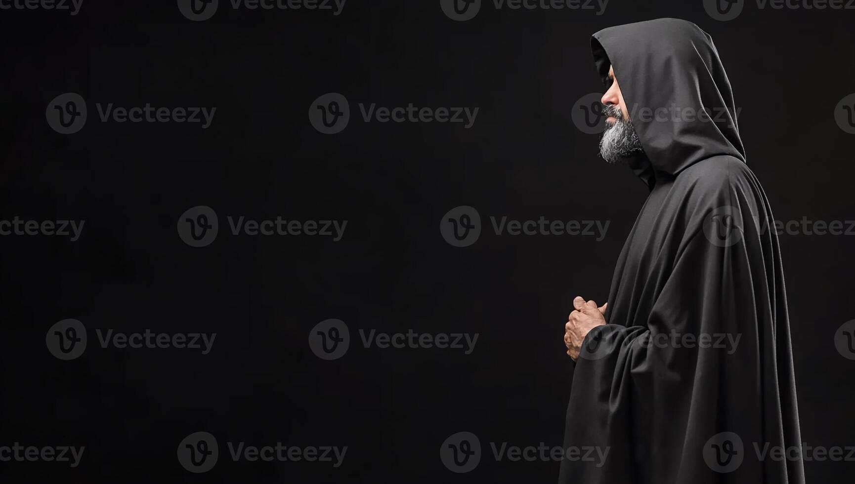 A solemn figure in a hooded cloak, set against a dark background. photo