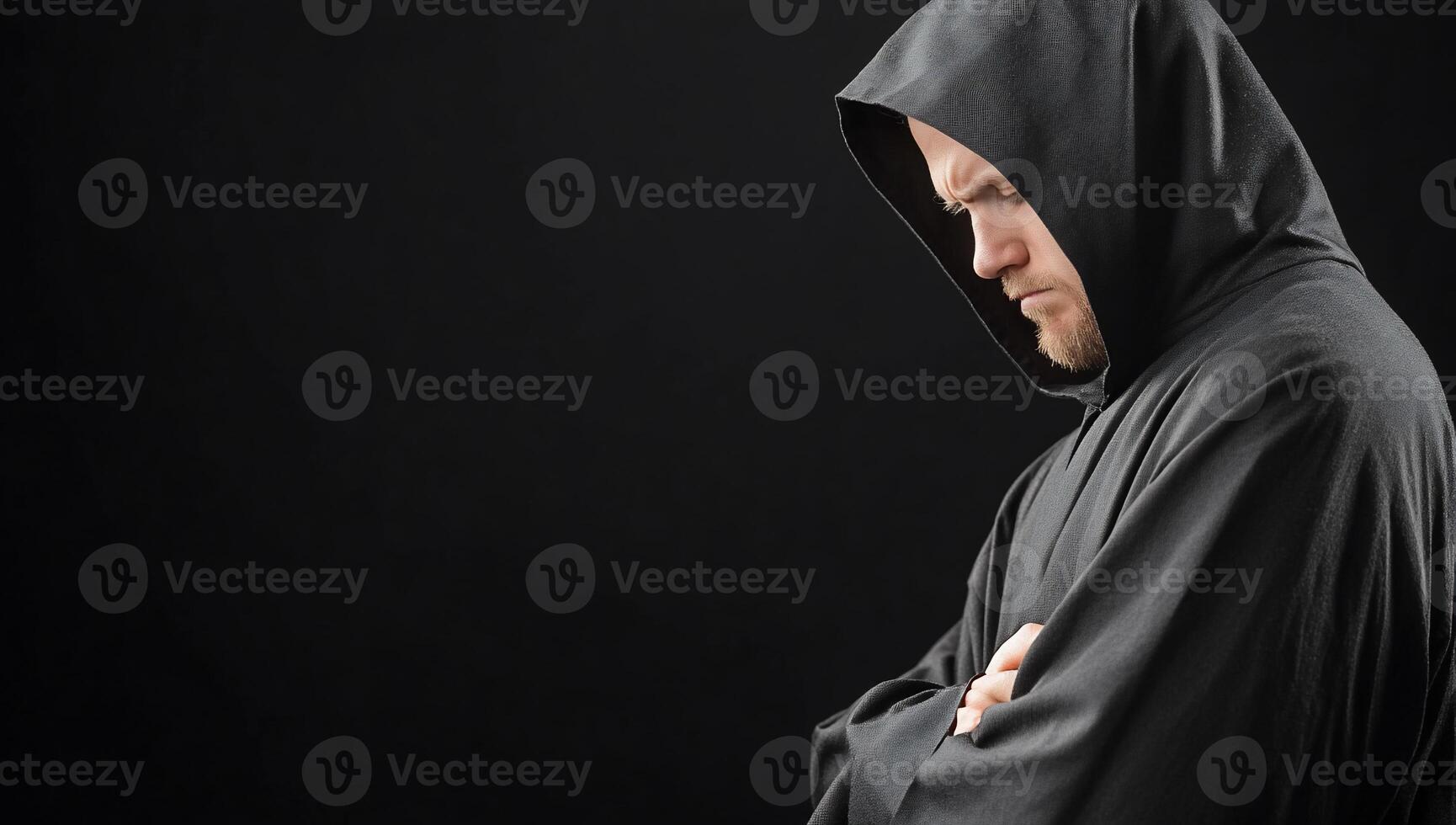 A hooded figure in contemplation against a dark background. photo