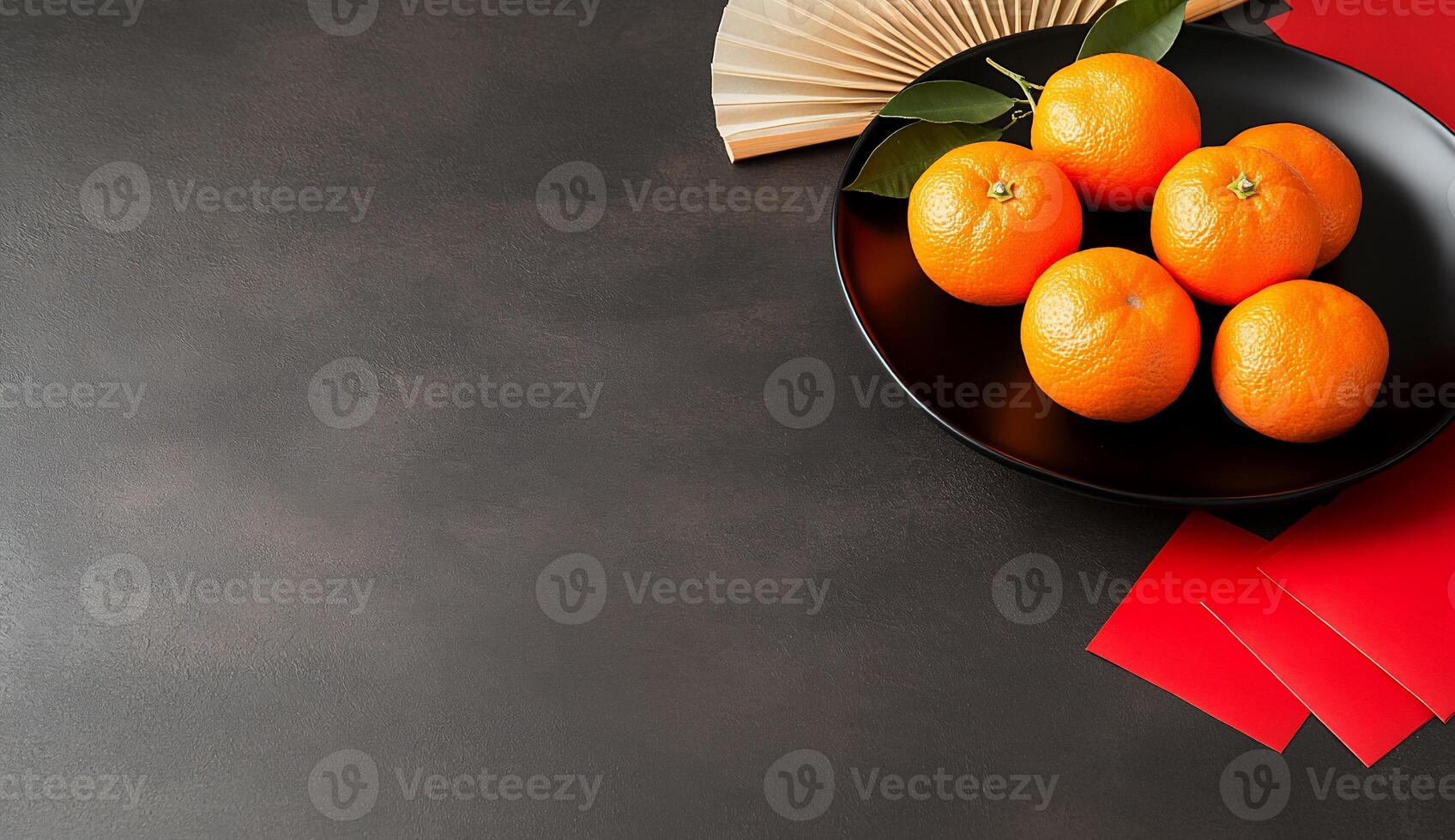 A black plate with oranges, red envelopes, and a fan on a dark surface. photo