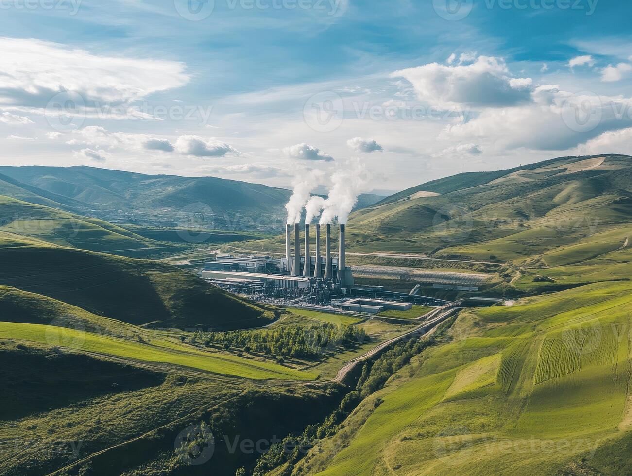 Aerial view of a power plant with smoke stacks surrounded by green hills and a clear blue sky. photo