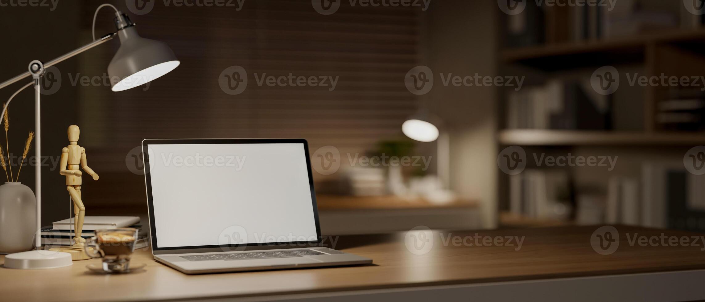 A White screen laptop on wooden table with decor, with blurry background of study room in dim light. photo