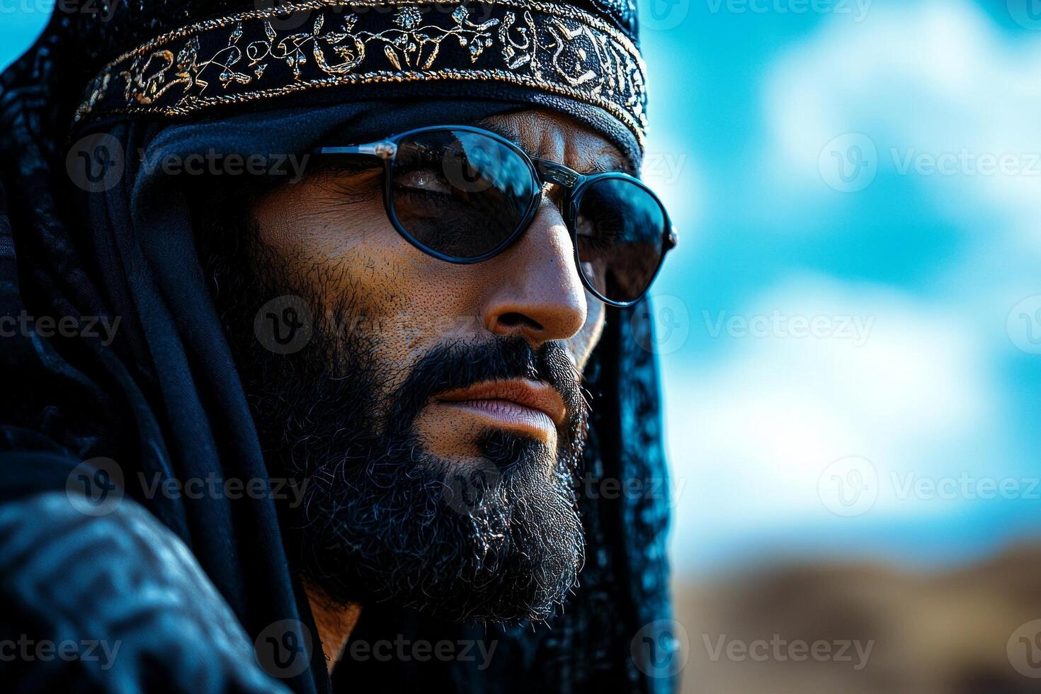 man dressed in dark blue jubba and taqiyah cap stands in open desert landscape. wind subtly lifts fabric of his robe reflecting serene moment of celebration photo