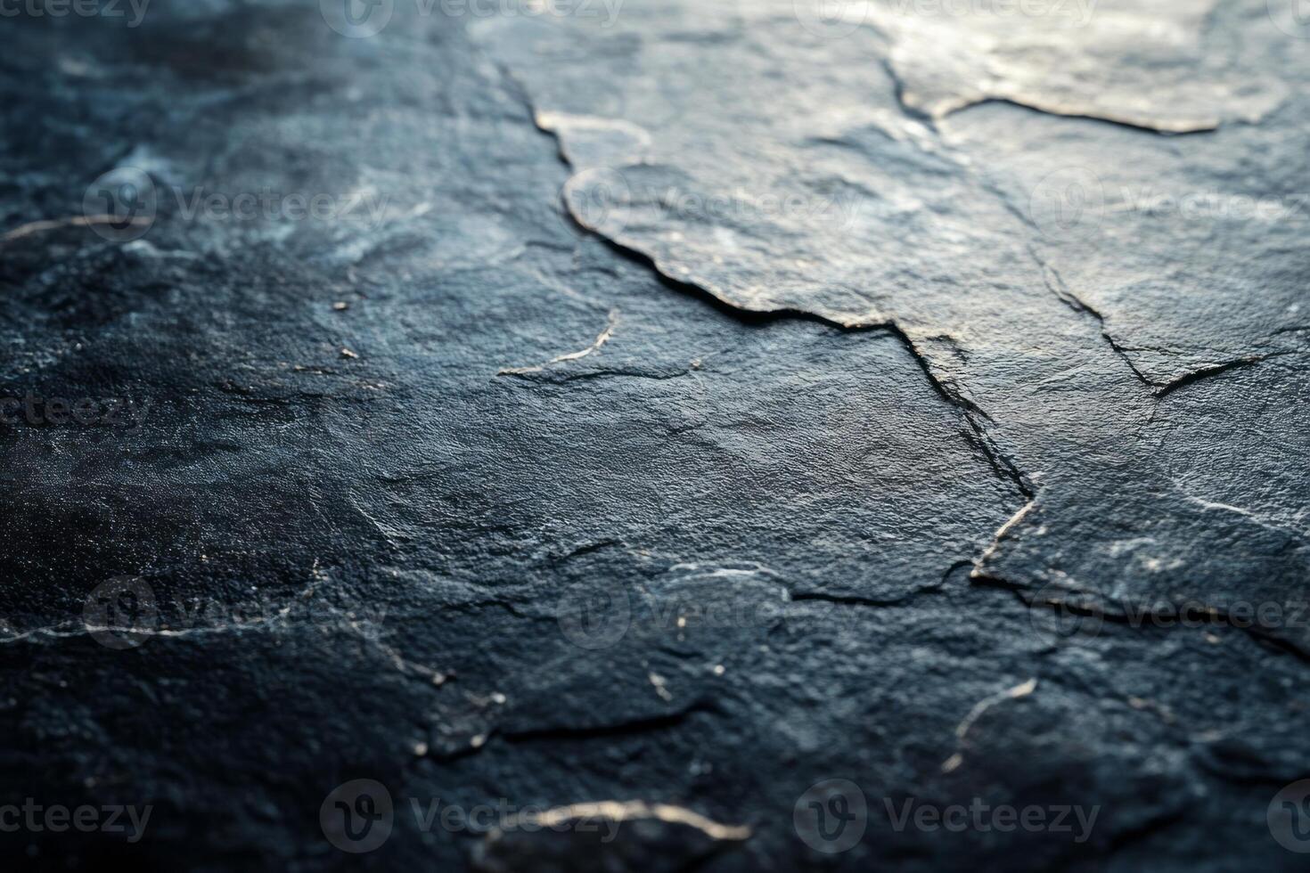 Close-up of a textured, dark stone surface with natural cracks and highlights, creating a dramatic and rugged appearance. photo