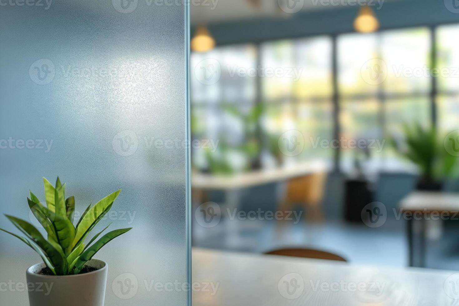 A small green plant in a pot with a blurred modern office background featuring large windows and natural light. photo