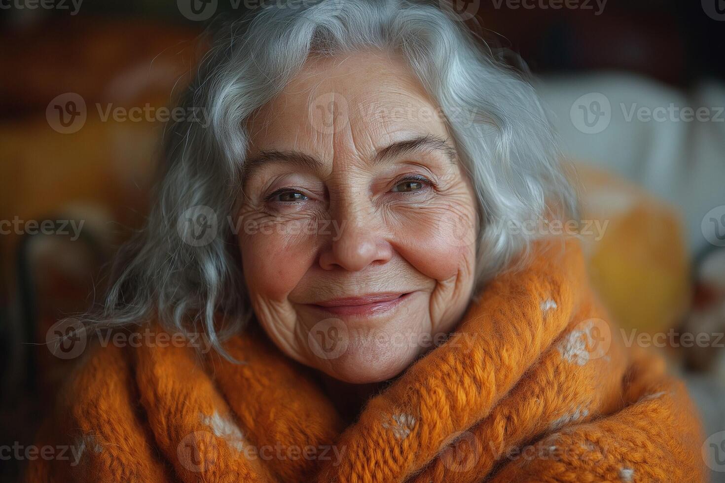 Smiling elderly woman with gray hair wrapped in an orange blanket, exuding warmth and serenity. photo