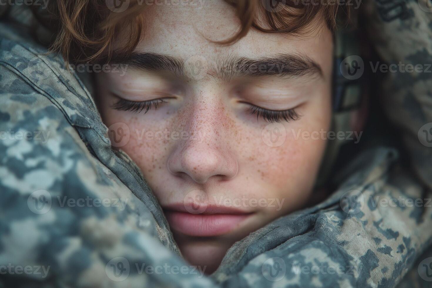 A young male soldier with freckles rests peacefully in camouflage gear, showcasing a moment of calm amidst the chaos of military life. photo