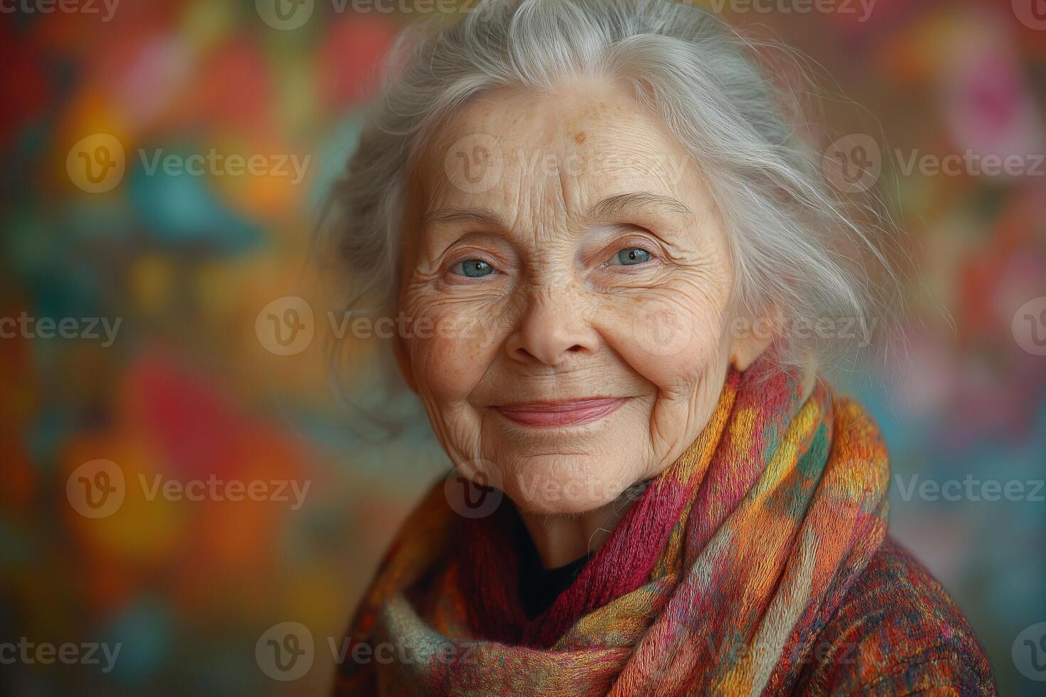 Elderly Caucasian woman with gray hair and a colorful scarf, smiling warmly against a vibrant background. photo