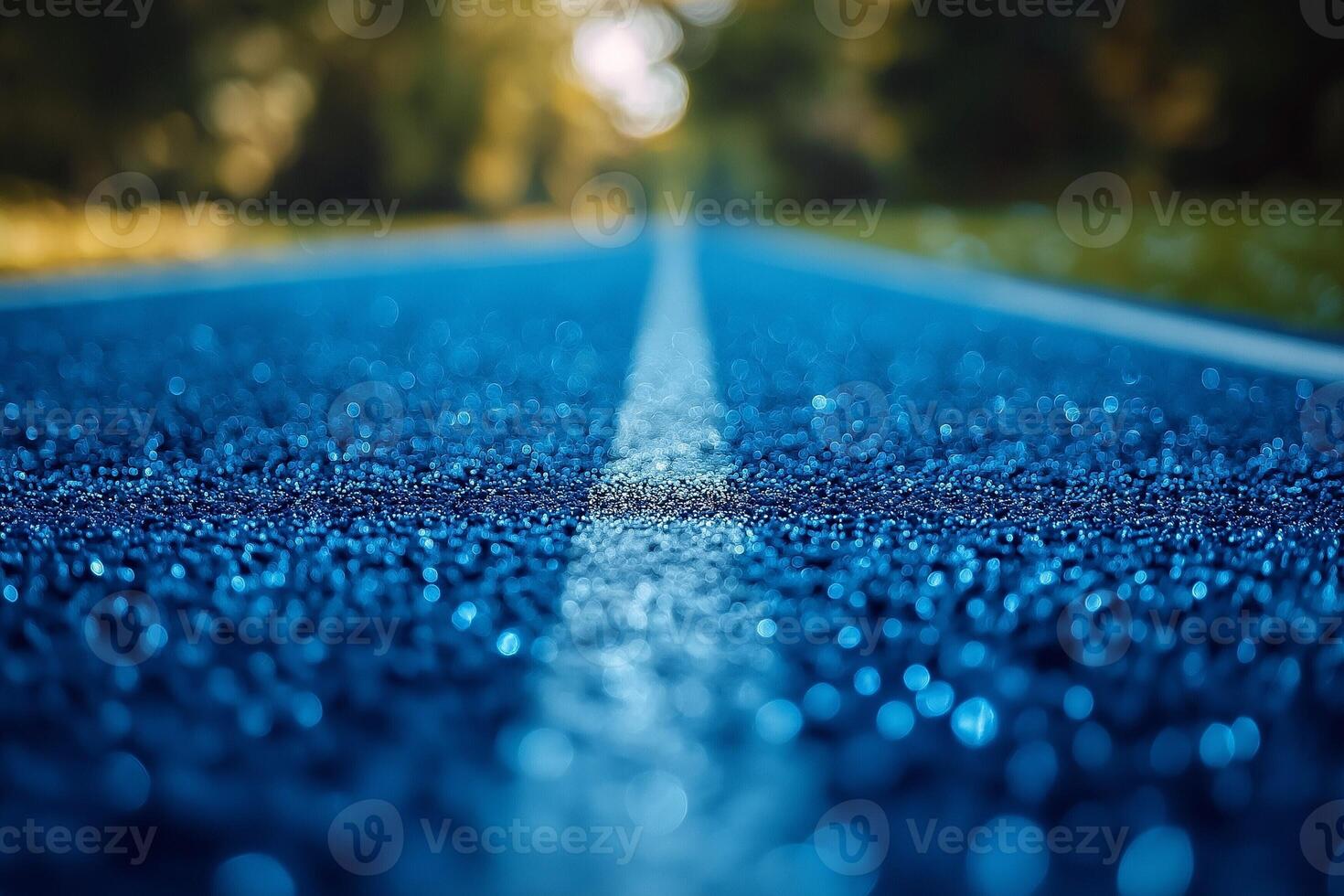 A vibrant blue running track glistens with dew, stretching into the distance under a soft, blurred background of greenery. photo