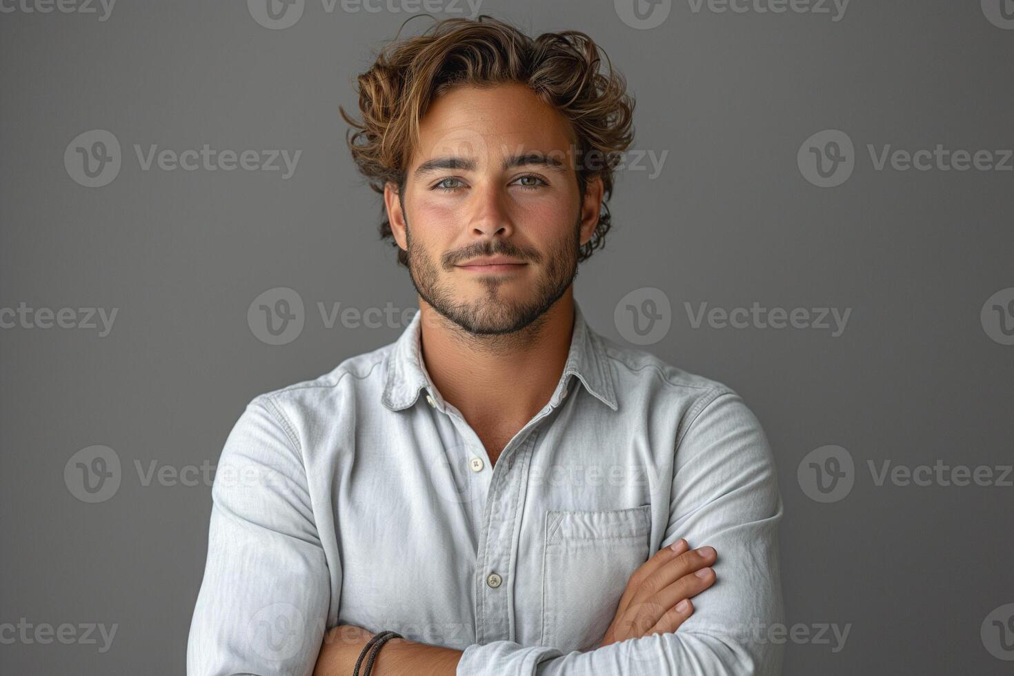 Confident young man with wavy hair and beard, exuding charm against a neutral gray background. photo
