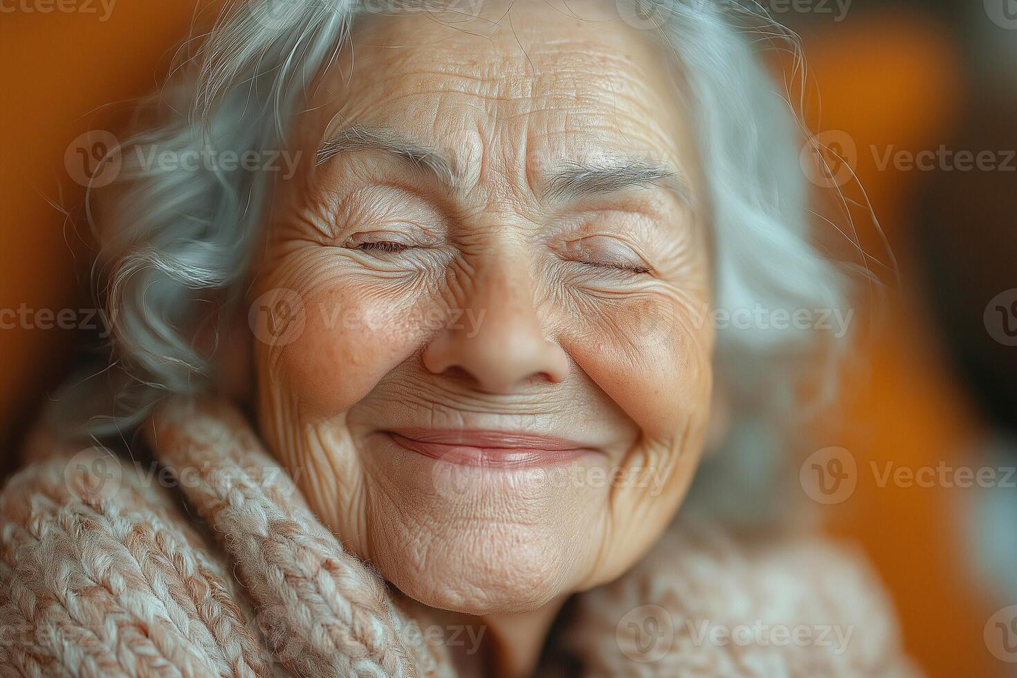 A joyful elderly woman with silver hair smiles warmly, wrapped in a cozy, knitted sweater, radiating happiness and warmth. photo
