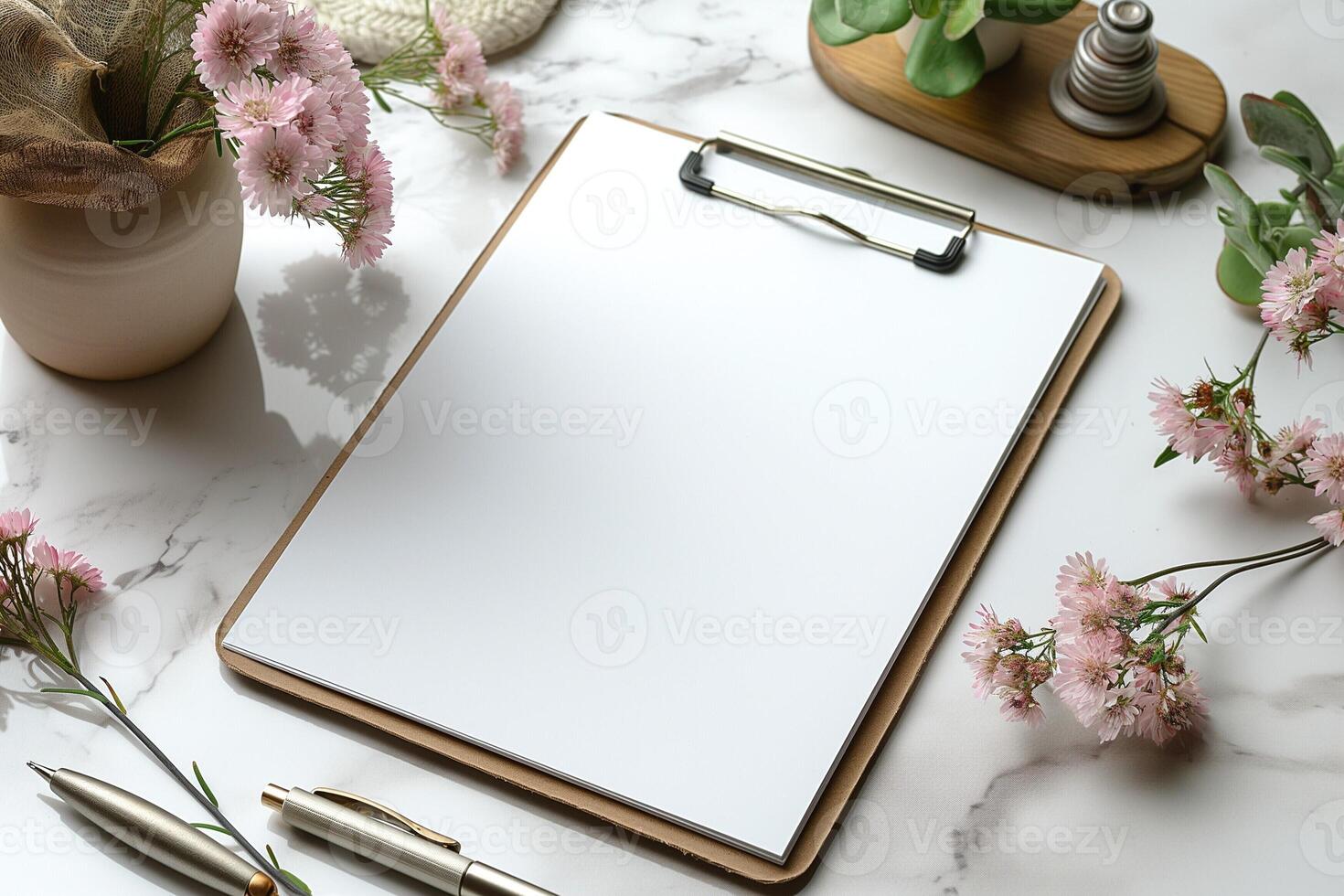 A serene workspace featuring a blank clipboard surrounded by soft pink flowers and elegant stationery. photo