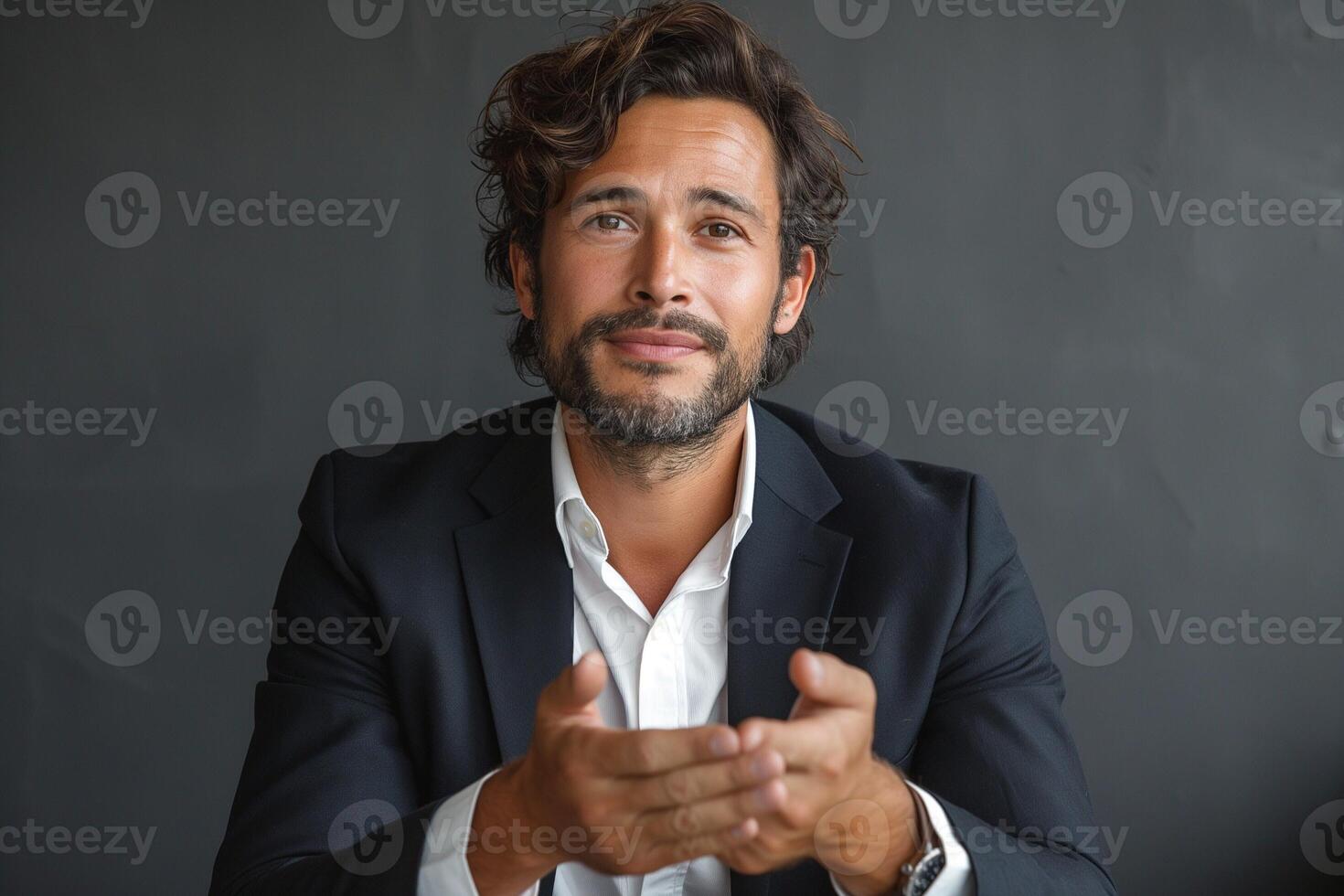 A confident Hispanic man in a suit gestures with his hands, engaging in conversation with a thoughtful expression. photo