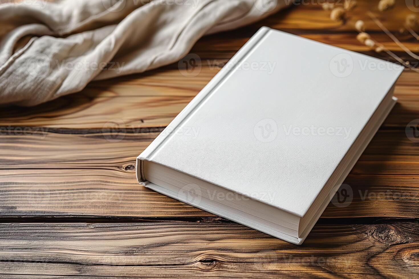 A blank white book resting on a rustic wooden table, surrounded by soft fabrics and dried flowers. photo