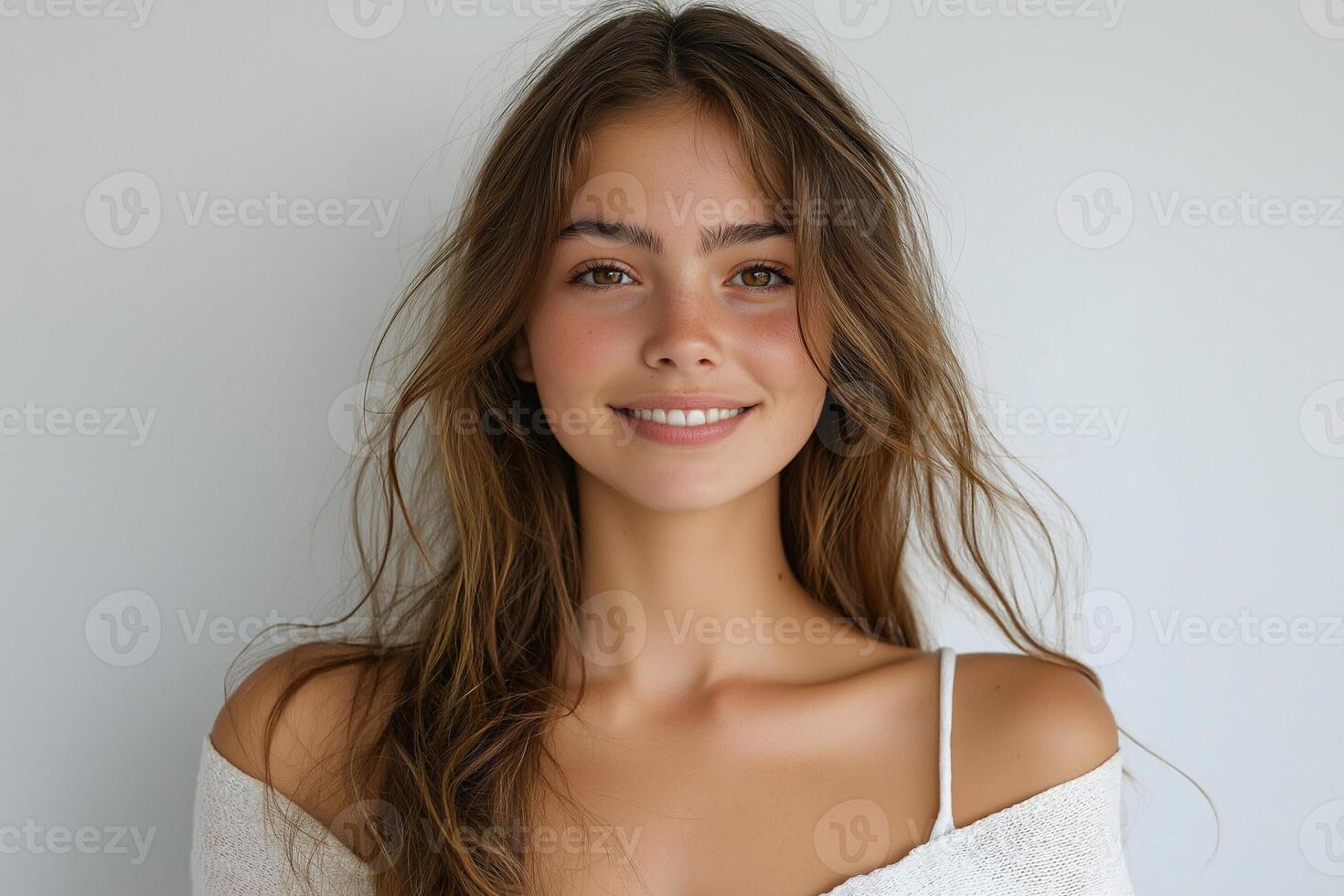 A young woman with long, wavy hair and a bright smile, dressed in a cozy white top against a light backdrop. photo