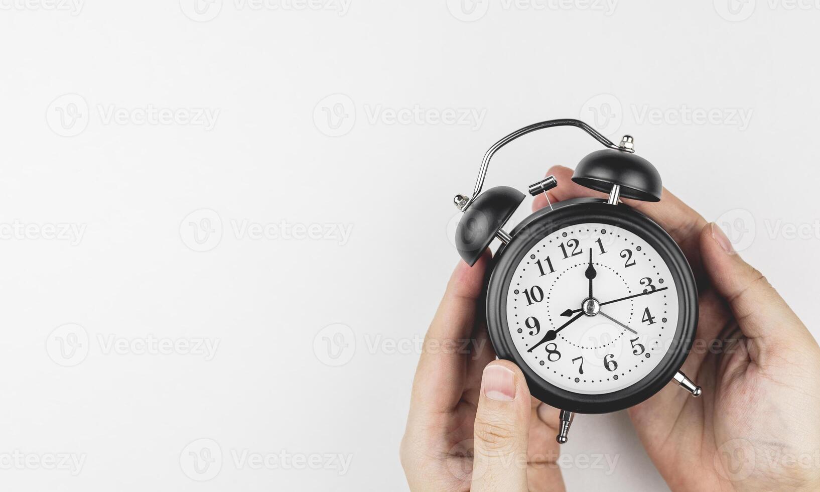 Hand holding a black alarm clock on white background, with copy space. Concepts of time management, appointment hours, and overtime. photo