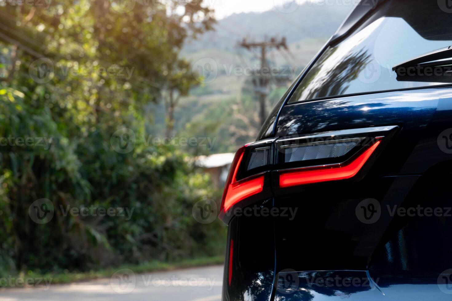 Rear side of dark with turn on brake light. side of car on aspahlt road with tree and grass in the countryside. photo