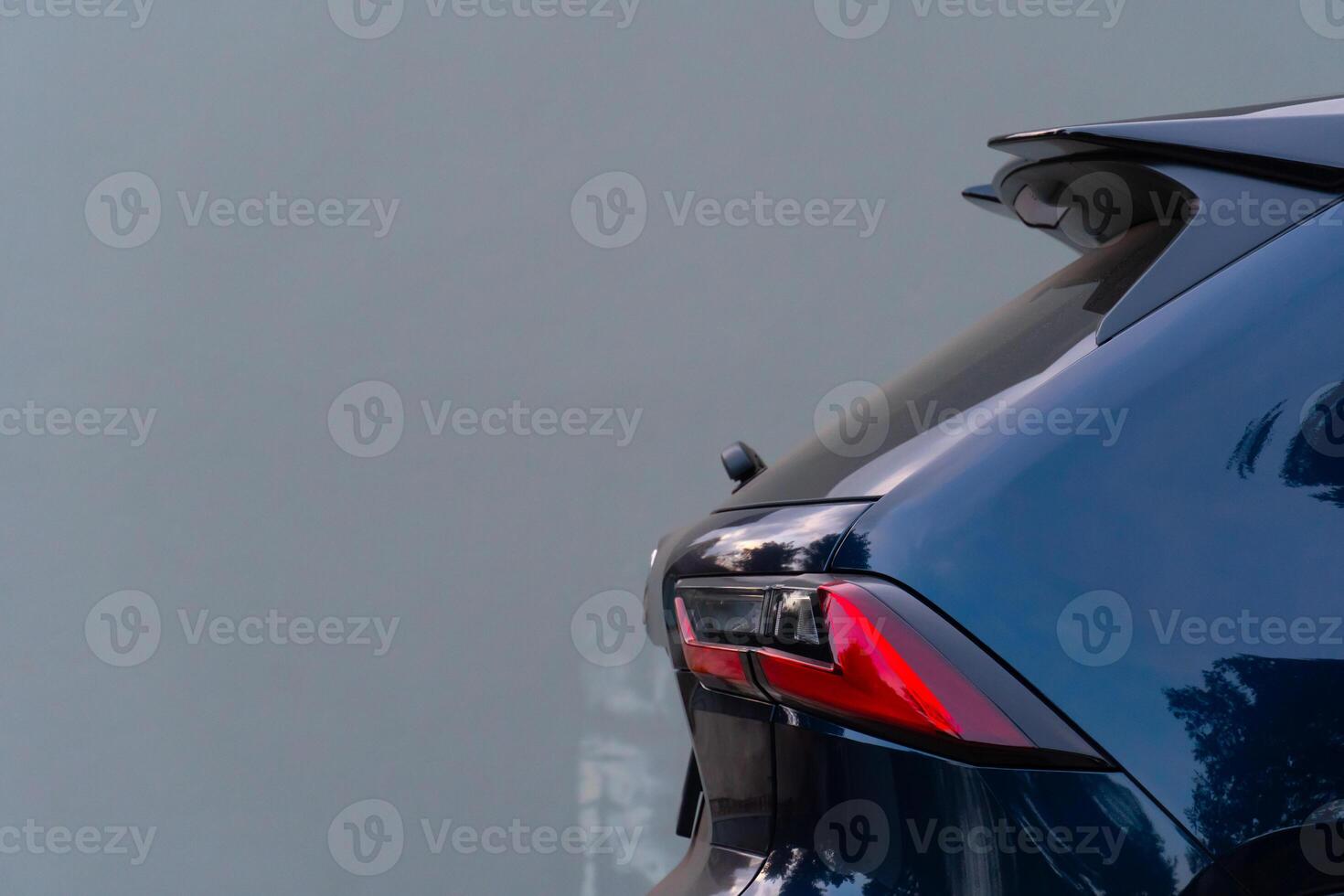 Partial rear view of a dark blue black SUV. Possibly based on the taillight design. The car is parked against a plain light-colored background. photo