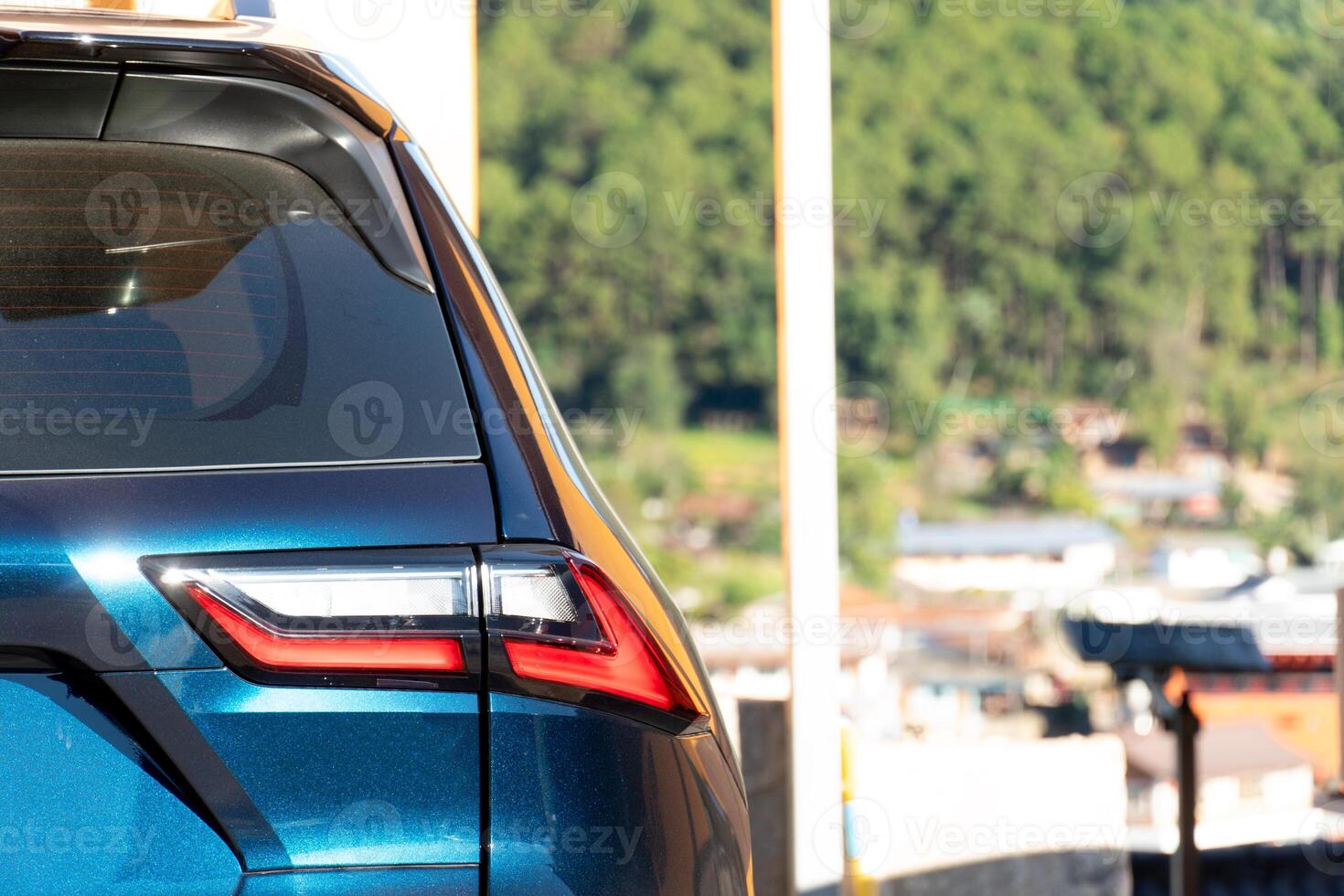 Close up of the rear of a blue car. Background shows greenery and buildings suggesting a mountainous or hilly area. Environment at day time. photo