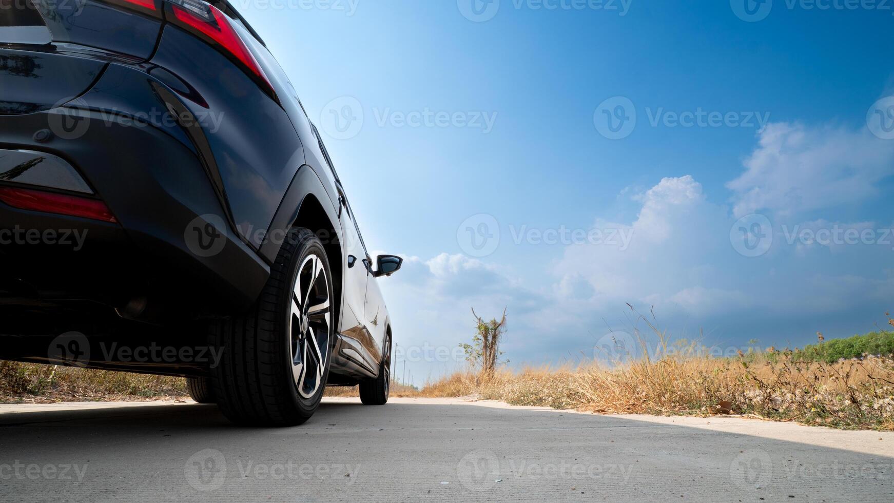 Modern SUV parked on a rural road. Landscape of dry grass and a clear blue sky dotted with fluffy clouds. Scene evokes a sense of freedom and adventure suggesting a road trip or journey. photo