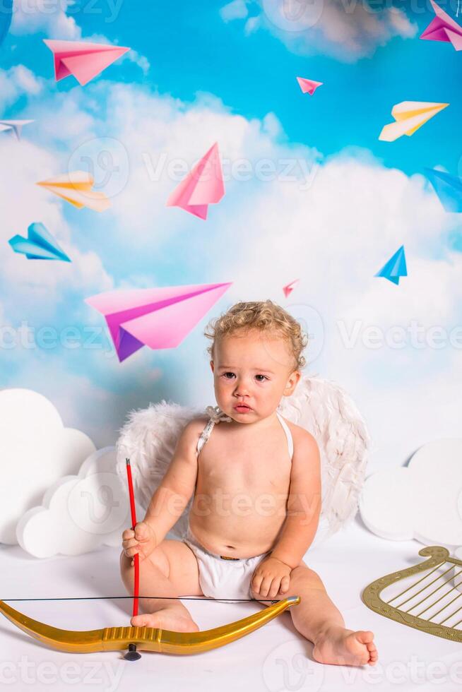 A baby sitting on a bed with an angel wings and bow photo