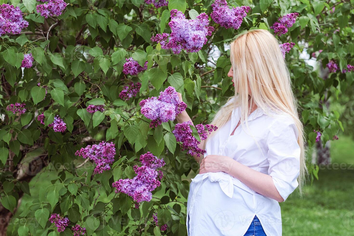 A pregnant woman is standing in front of a tree with purple flowers photo
