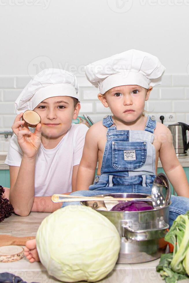 Two children in chef hats sitting on a table with vegetables photo