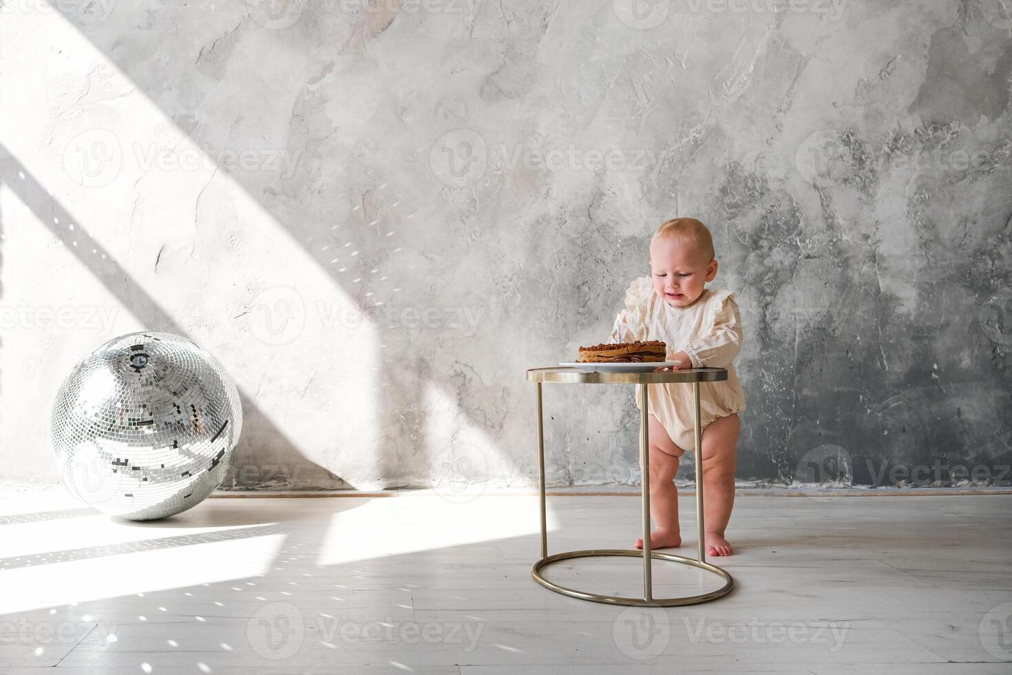 A baby is standing on a table with a cake photo
