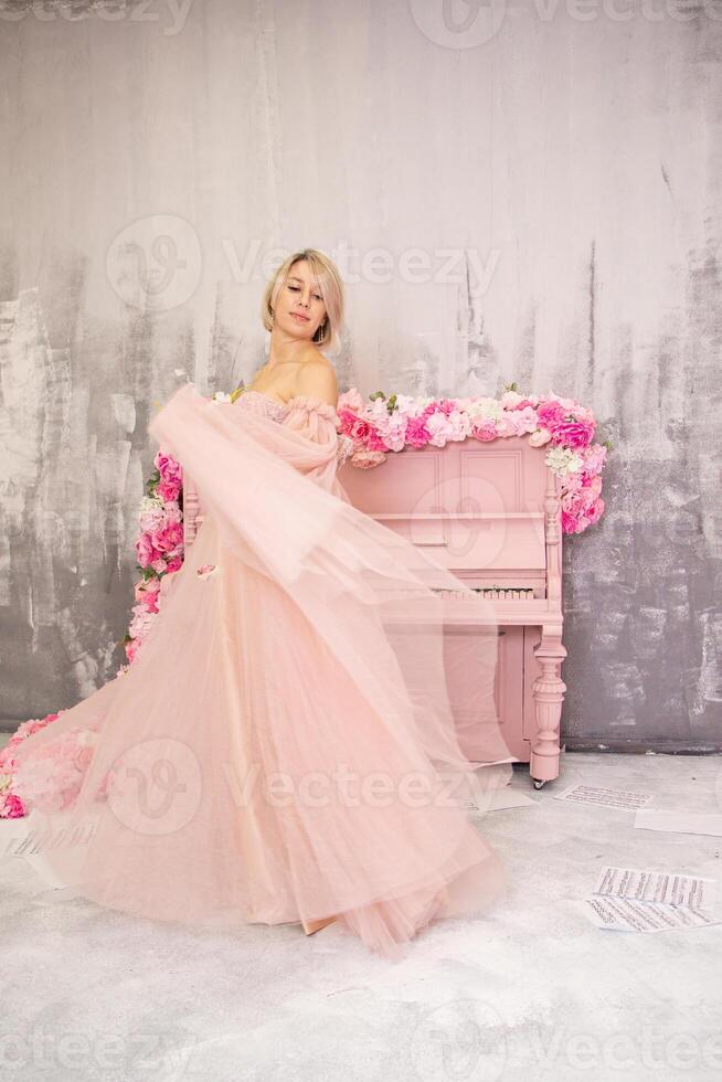 A woman in a pink dress posing in front of a piano photo