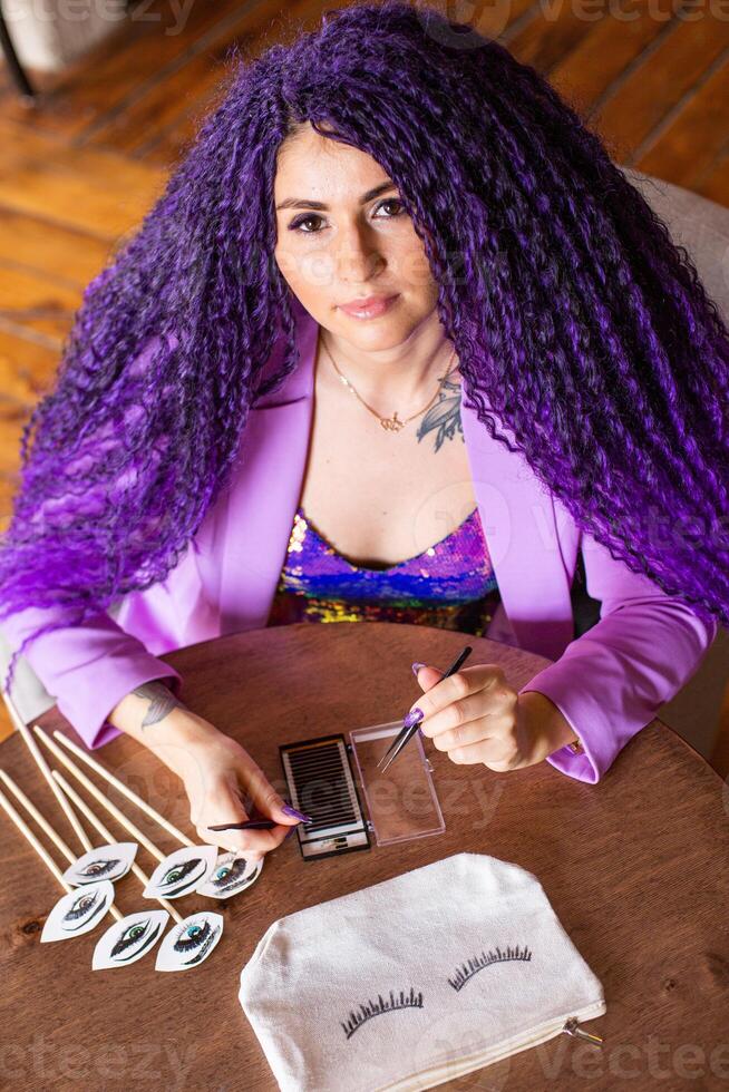 A woman with purple hair sitting at a table with some makeup photo