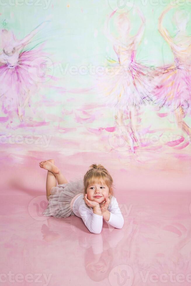 A little girl laying on the floor with a pink background photo