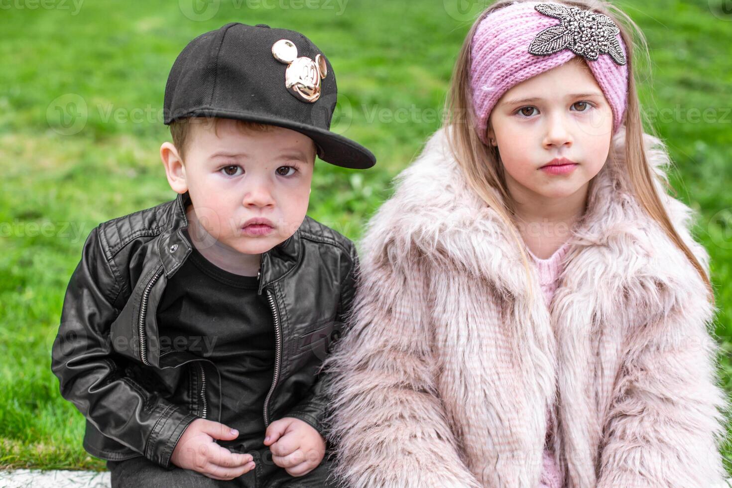Two children wearing hats and coats sitting on the ground photo