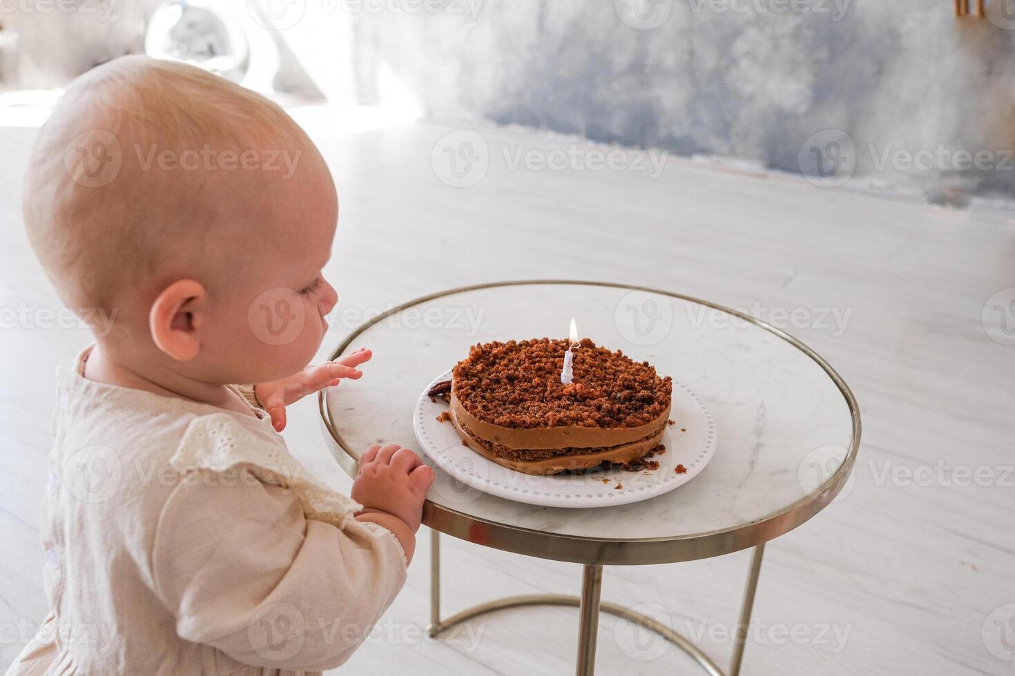 A baby sitting at a table with a cake with a candle photo