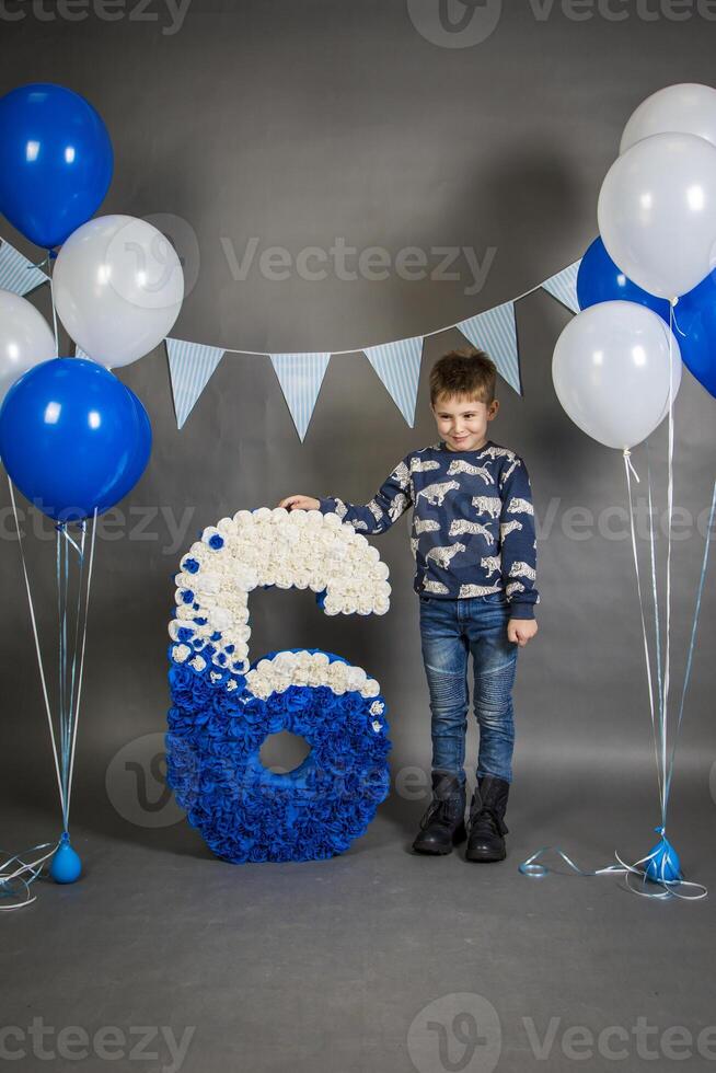A young boy standing next to a large blue and white number six photo