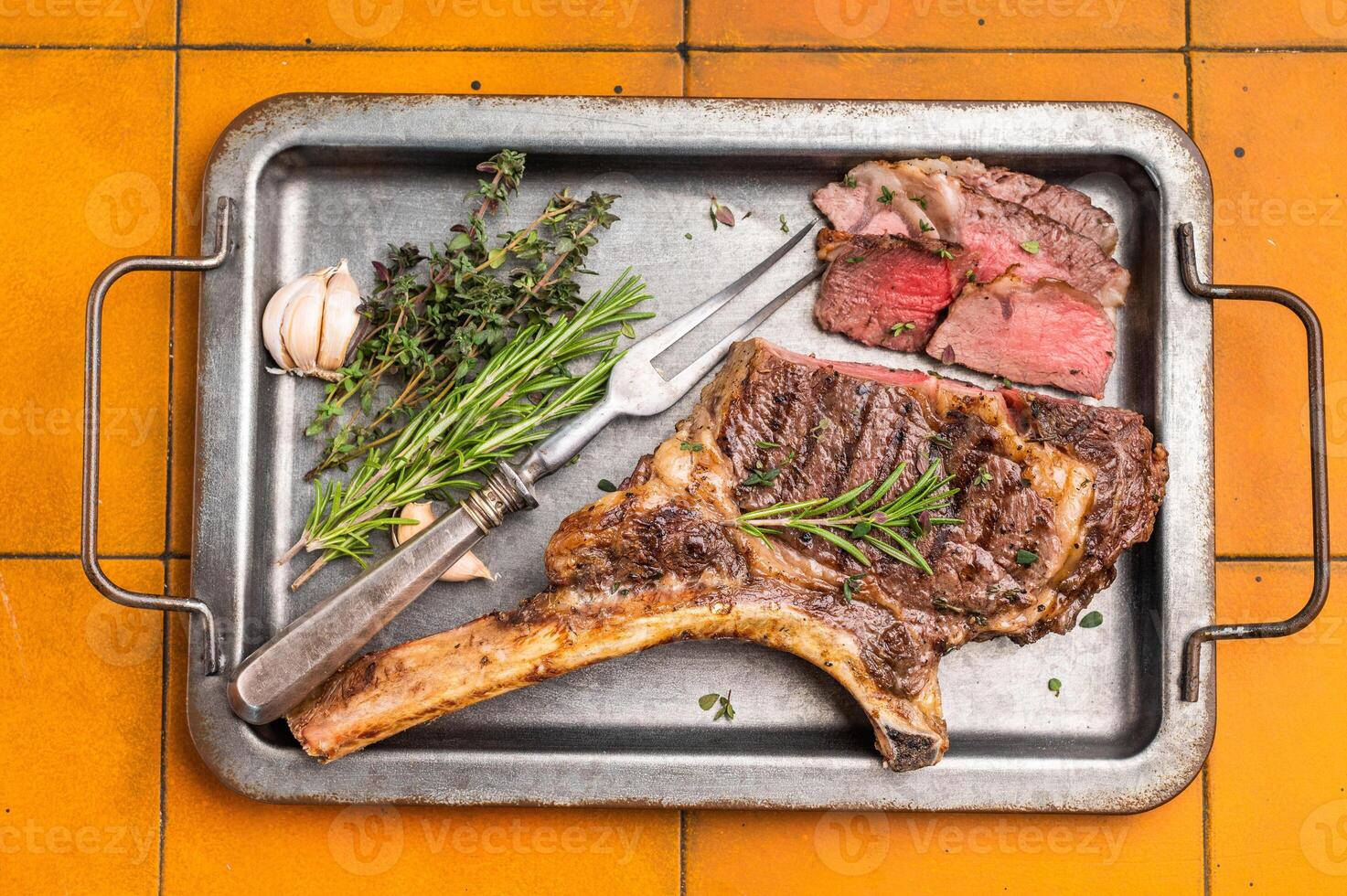 BBQ cooked Tomahawk beef steak, prime ribeye with bone on tray with herbs. dark background. top view photo