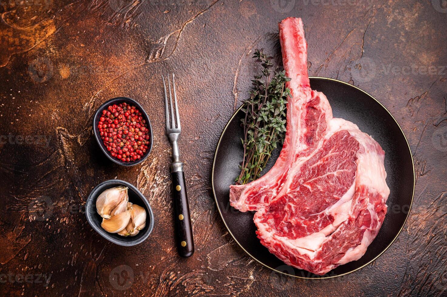 Fresh Tomahawk beef steak, raw marbled rib eye with bone on plate with herbs. brown background. top view photo