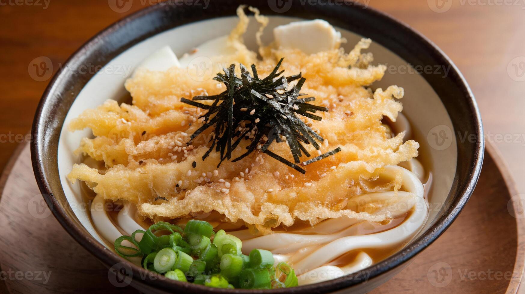 Delicious bowl of udon noodles topped with crispy tempura and garnished with green onions. photo