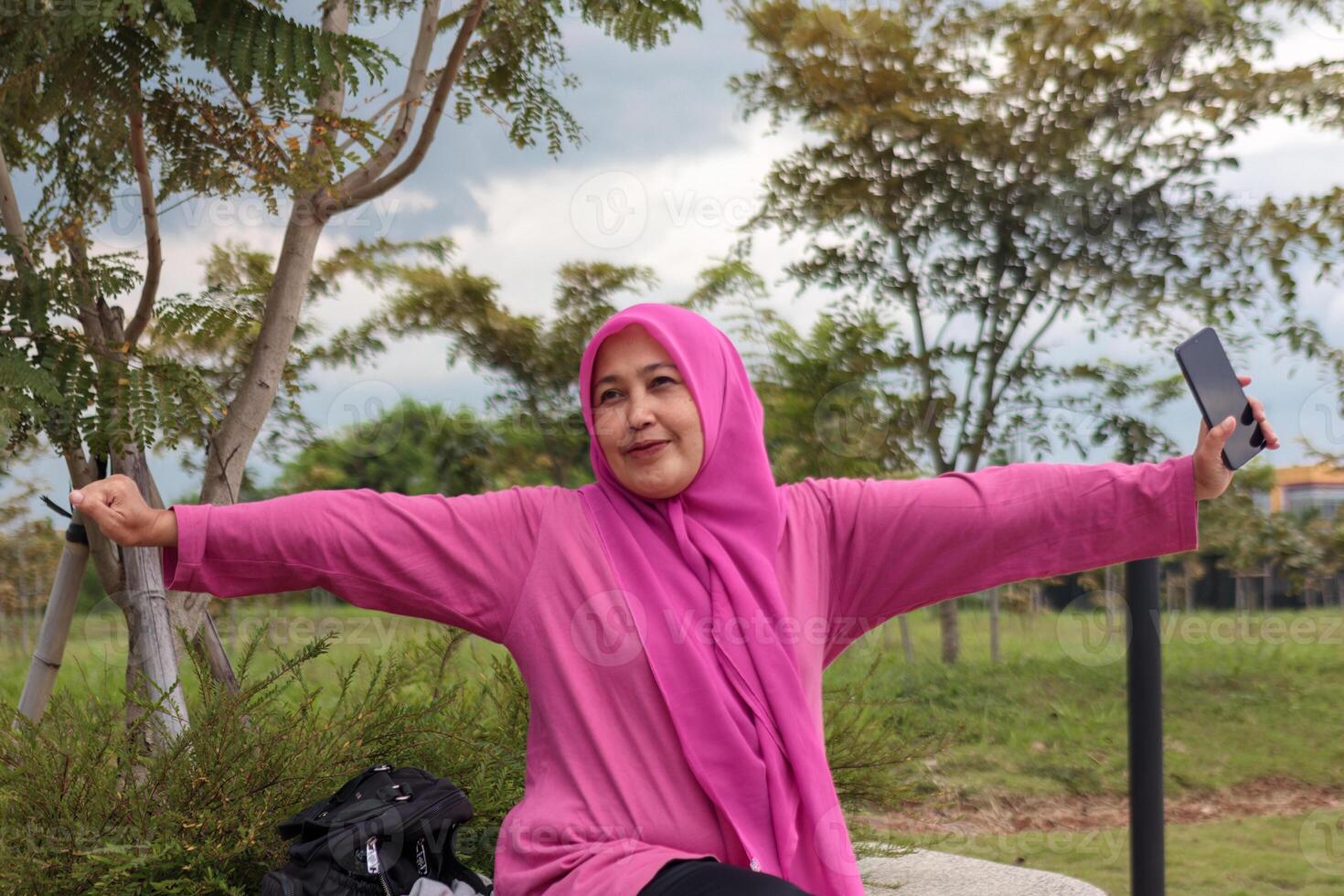 Cheerful Muslim Woman in Pink Hijab Spreading Arms in a Park photo