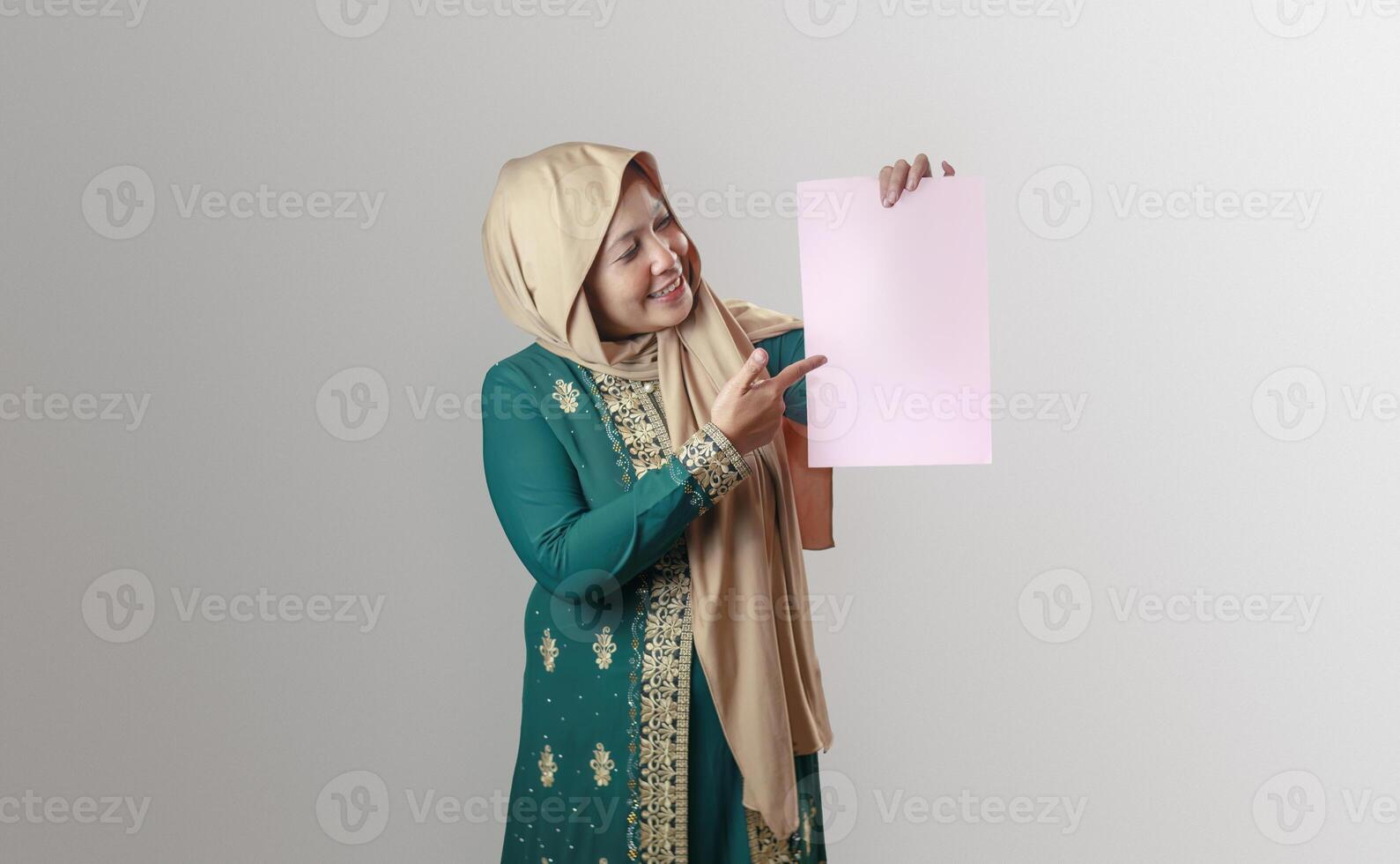 Smiling Muslim Woman Holding a Blank Paper Against a Neutral Background photo
