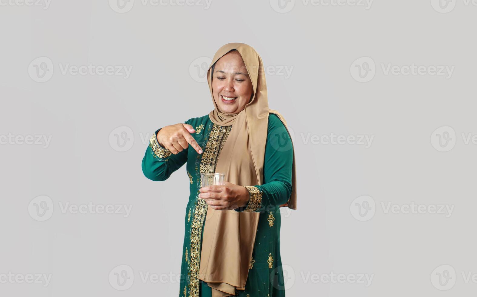 Smiling Muslim Woman Pointing at a Glass of Water in Traditional Outfit photo