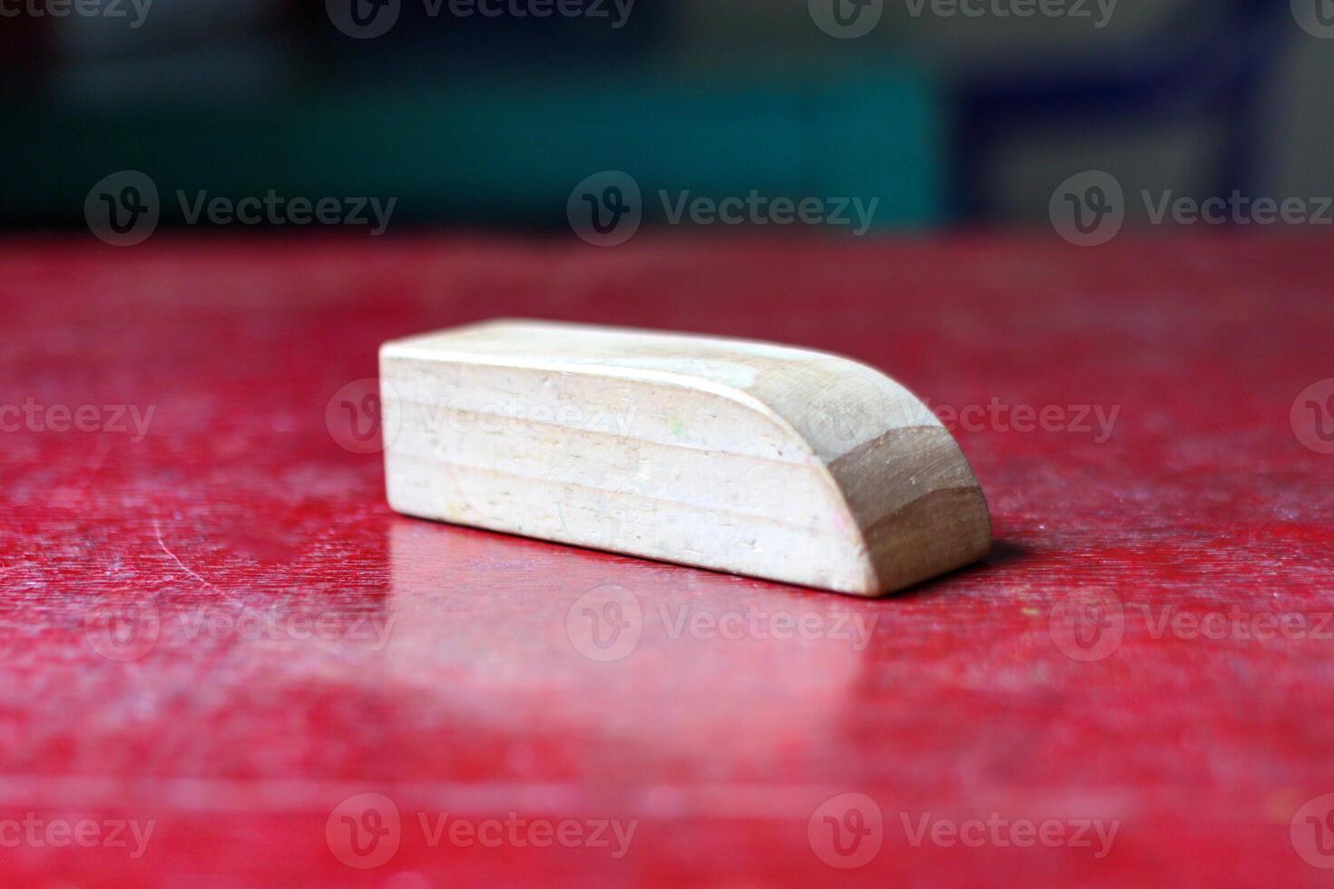 A smooth wooden block with a curved edge rests on a scratched red surface, creating a rustic yet minimalistic aesthetic photo